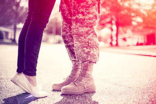 Woman hugging a soldier shown from the knees down