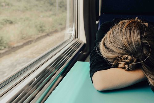 woman sitting by the window in a train with her head down on a table.