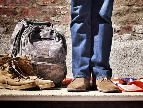 a person standing between boots and a backpack and an american flag