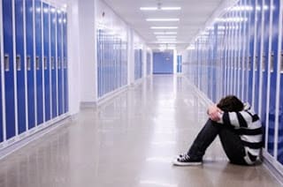 depressed kid sitting alone on the floor in a school hallway