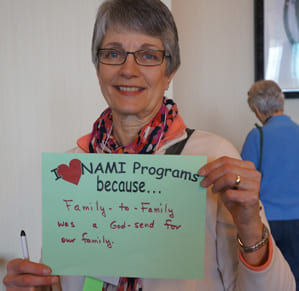 woman holding up a paper that says I heart NAMI Programs because...Family-to-Family was a Godsend for our family