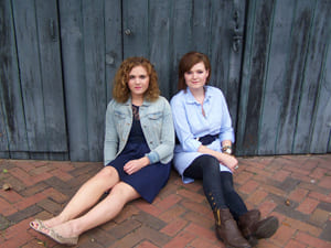 two women sitting on the ground against a wall