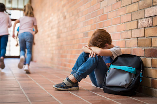 young boy sitting on the floor at school with his head down crying