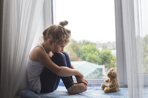little girl sitting on a window sill looking at a teddy bear