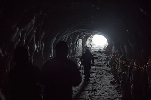 people walking through a dark tunnel with a bright light at the end