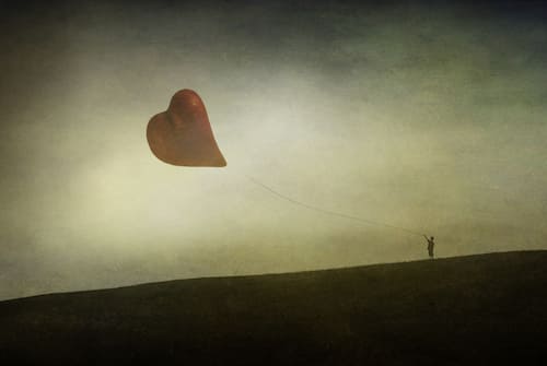 a person on a hillside flying a kite in the shape of a heart