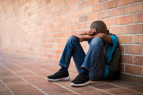 student sitting against a brick wall with his head down