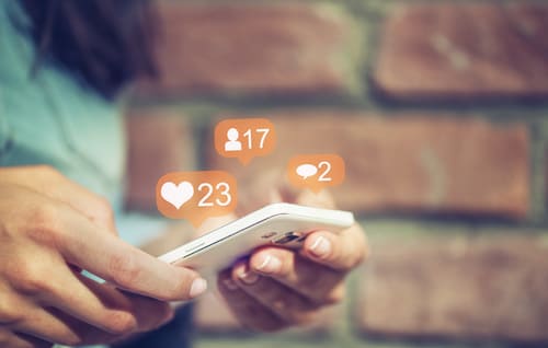 hands on a smart phone with social icons floating above the phone