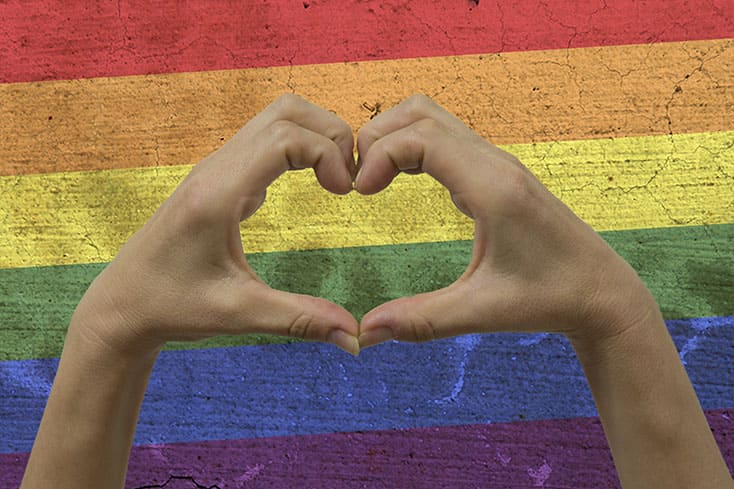 heart hands in front of rainbow flag